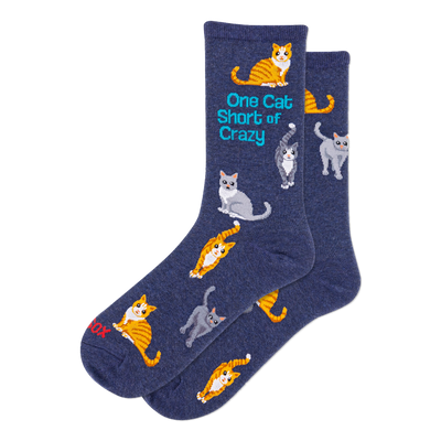 Two navy blue crew socks with a pattern of orange tabby and grey cats in various poses. One sock features text: 'One Cat Short of Crazy'.