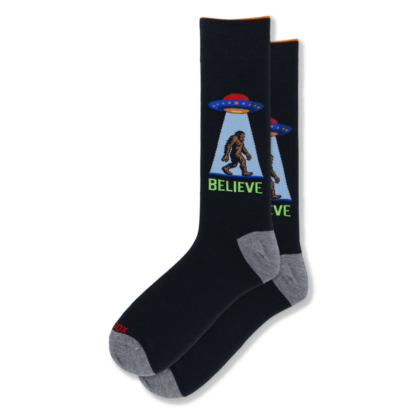 Black crew socks featuring a retro UFO beaming up Bigfoot in a blue light cone with the word BELIEVE in bright green text.