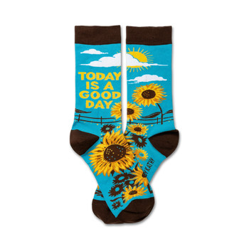 Pair of crew socks. Teal background with sunflowers, a sun, and the text 'Today is a good day'. Brown cuff.