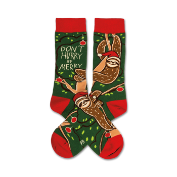  green christmas crew socks with red cuffs and toes. brown sloths wear red santa hats and hang from a branch with green leaves and red ornaments. text on the sock toes says 'don't hurry be merry'.  