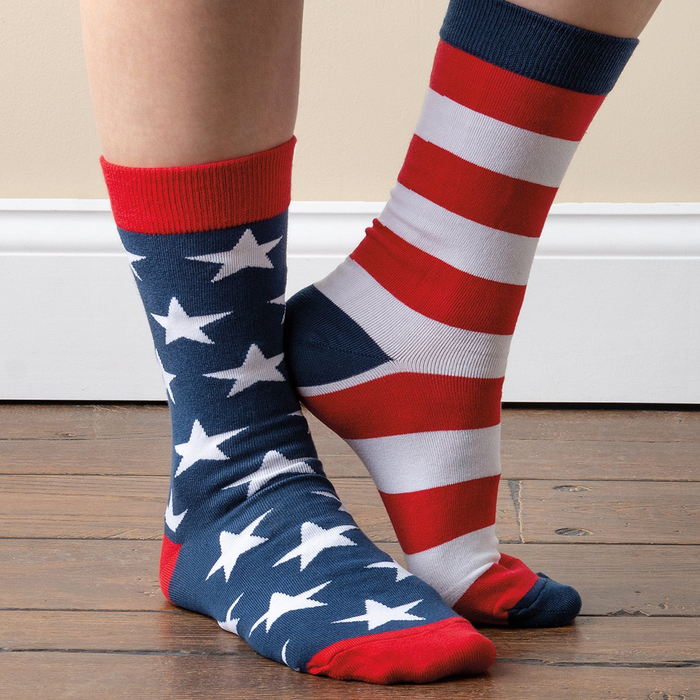 A person stands on a wooden floor wearing the mismatched stars and stripes crew socks. Left foot has stars, right has stripes.