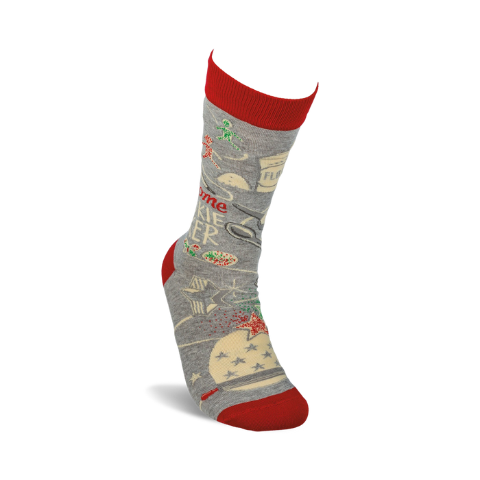 A pair of gray socks with a red toe, heel, and cuff. The socks have a pattern of Christmas trees, presents, and snowflakes. The words 