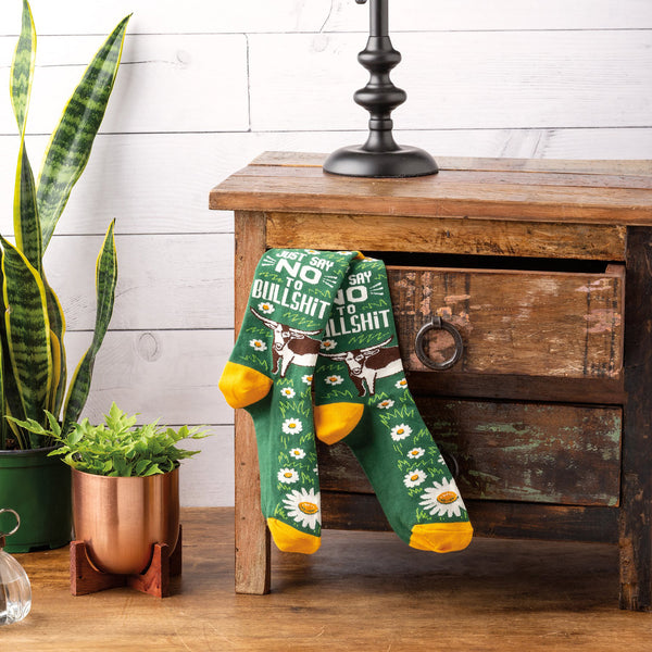 Lifestyle product shot showing 'Just Say No To Bullshit' socks casually displayed on a wooden side table. [lf]