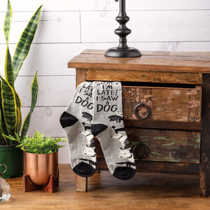 Pair of grey socks with dog pattern and text hanging over a rustic wooden drawer, with a snake plant and a copper pot visible.