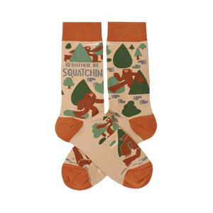 Pair of crew socks in beige, rust orange, and green, patterned with brown Sasquatch, trees, and 