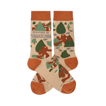 Pair of crew socks in beige, rust orange, and green, patterned with brown Sasquatch, trees, and "I'd Rather Be Squatchin'" text.