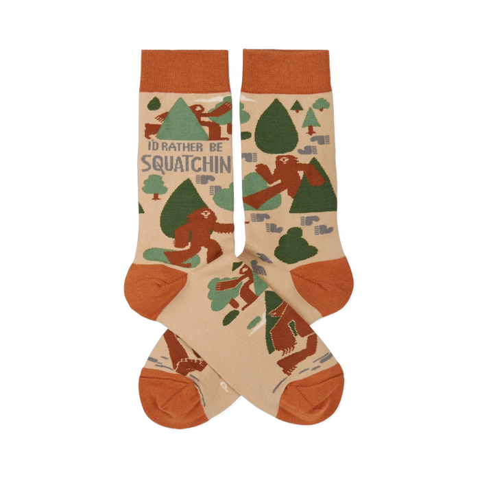 Pair of crew socks in beige, rust orange, and green, patterned with brown Sasquatch, trees, and 