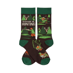 Pair of dark brown crew socks with green cuffs, heels, and toes. Pattern includes trees, deer, and hunters with rifles and bows. Text reads 'I'D RATHER BE HUNTING'.