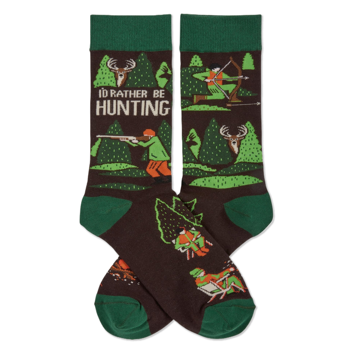 Pair of dark brown crew socks with green cuffs, heels, and toes. Pattern includes trees, deer, and hunters with rifles and bows. Text reads 'I'D RATHER BE HUNTING'.