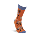 Single orange crew sock standing upright, with blue cuff, heel, and toe, showing "Studmuffin" text and cartoon muffins.