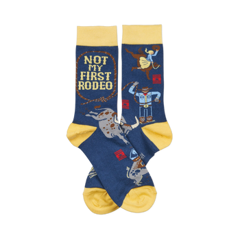 Pair of dark blue crew socks with yellow cuffs, heels, and toes. Design includes cowboys, bulls, and "NOT MY FIRST RODEO" text.