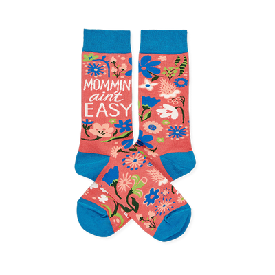 Two coral pink crew socks with blue cuffs, heels, and toes, featuring a colorful floral pattern and "MOMMIN' AIN'T EASY" text.