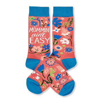 Two coral pink crew socks with blue cuffs, heels, and toes, featuring a colorful floral pattern and "MOMMIN' AIN'T EASY" text.