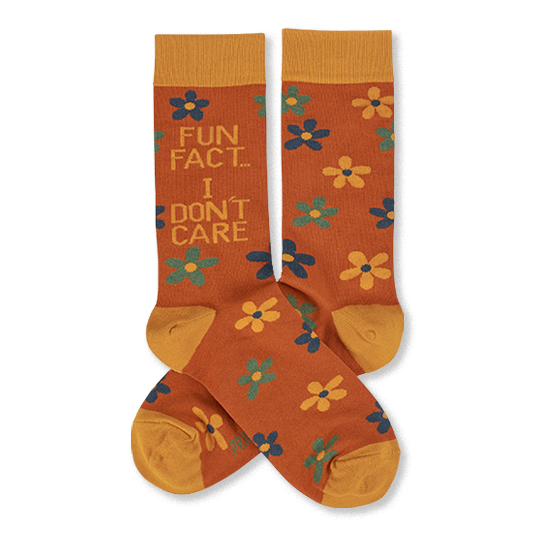 Pair of crew socks in rust orange with yellow cuffs, heels, and toes. Features scattered yellow, teal, and blue flowers. One sock reads 'FUN FACT... I DON'T CARE' in blue and teal text.