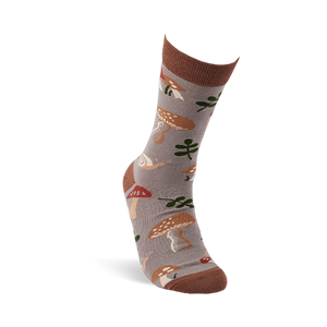 A single greyish-brown crew sock, worn on a foot, featuring mushrooms, leaves, and snails. Dark brown cuff, heel, and toe.