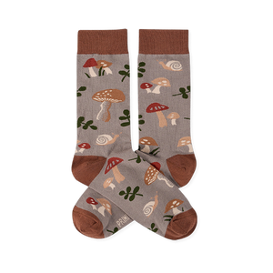 Two crew socks with a greyish-brown background, featuring a pattern of brown and red mushrooms, green leaves, and snails. Dark brown cuffs, heels, and toes.