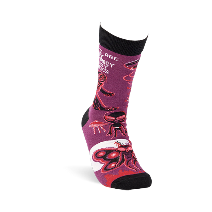 Single purple crew sock shown at an angle, featuring Mothman, alien, and UFO patterns with black cuff and toe.