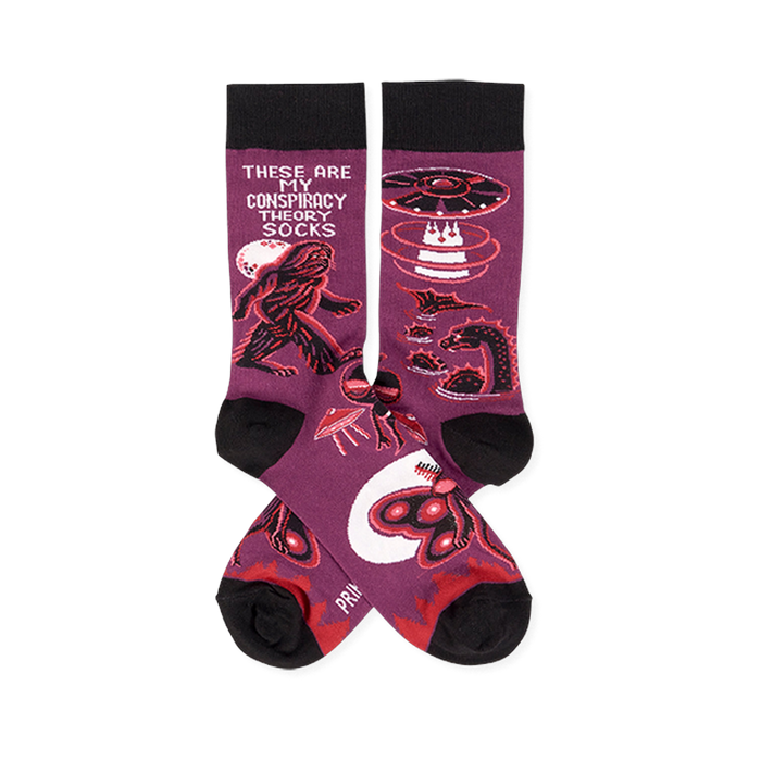 Pair of purple crew socks with black cuffs, heels, and toes, featuring Bigfoot, UFOs, aliens, and Mothman designs.