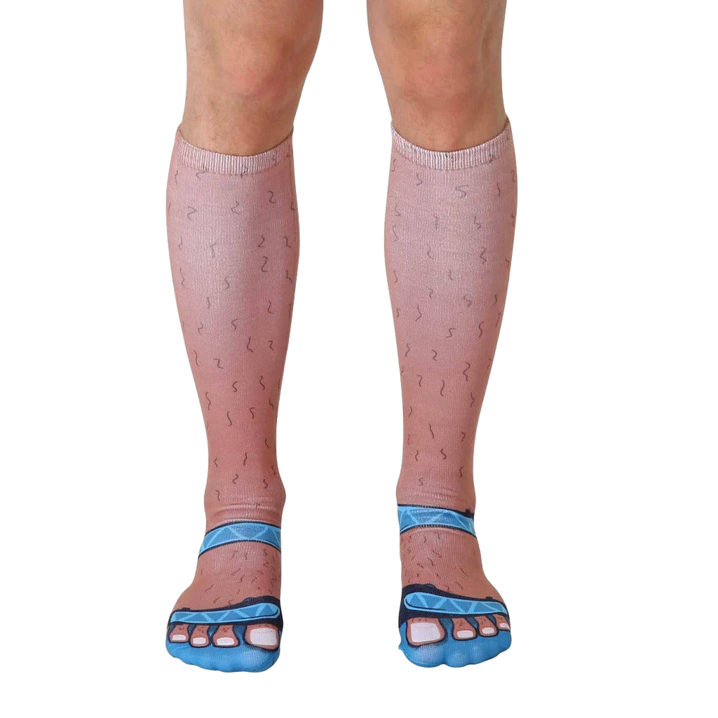 Pair of tan crew socks with printed hairy legs and blue sandals. Fun novelty socks for a quirky style statement. [lf]