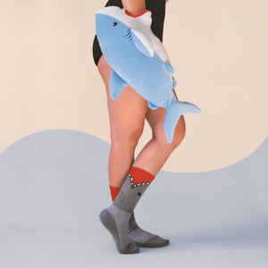 Lifestyle photo showing a person wearing the 'Bite Me' shark socks with a plush shark toy.