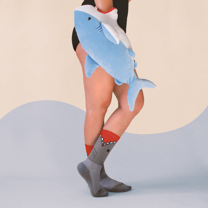 Lifestyle photo showing a person wearing the 'Bite Me' shark socks with a plush shark toy.