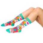 A person's legs, bent at the knees, wearing the green, pink, orange, and yellow floral 'Mother Of The Freakin' Year' crew socks on a white background.