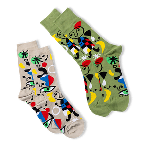 Two pairs of the same abstract art socks, one on a tan background and one on an olive green background, laid at an angle.