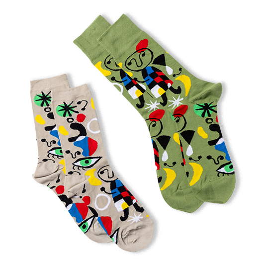 Two pairs of the same abstract art socks, one on a tan background and one on an olive green background, laid at an angle.