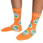 A person wearing a pair of orange crew socks featuring a ranch dressing bottle pattern, standing on a white background.