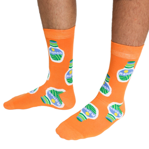 A person wearing a pair of orange crew socks featuring a ranch dressing bottle pattern, standing on a white background.