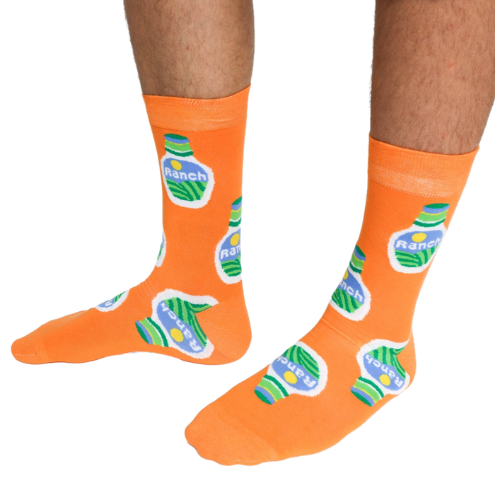 A person wearing a pair of orange crew socks featuring a ranch dressing bottle pattern, standing on a white background.