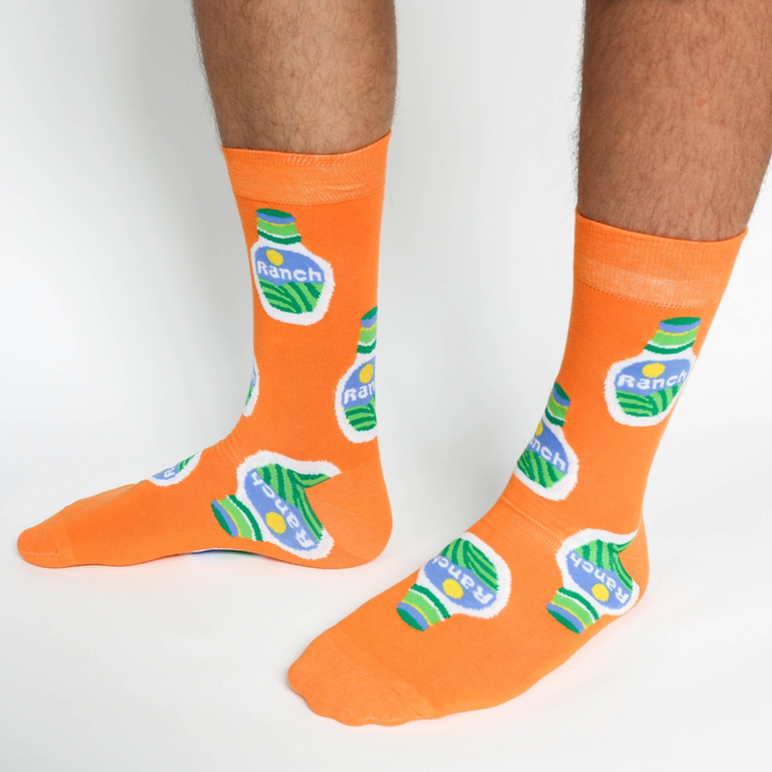A person wearing a pair of orange crew socks featuring a ranch dressing bottle pattern, standing on a white background.
