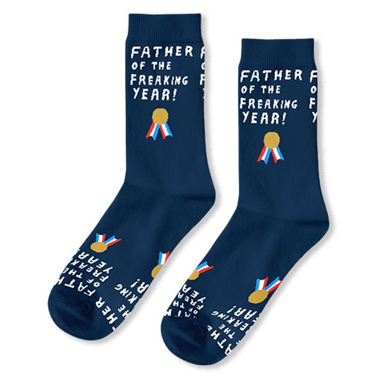 Flat lay of navy blue crew socks with white text reading FATHER OF THE FREAKING YEAR and a gold medal with colorful ribbons.
