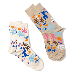 Two pairs of abstract art-patterned socks. One pair is tan, the other is cream, both with blue figures, faces, and shapes.