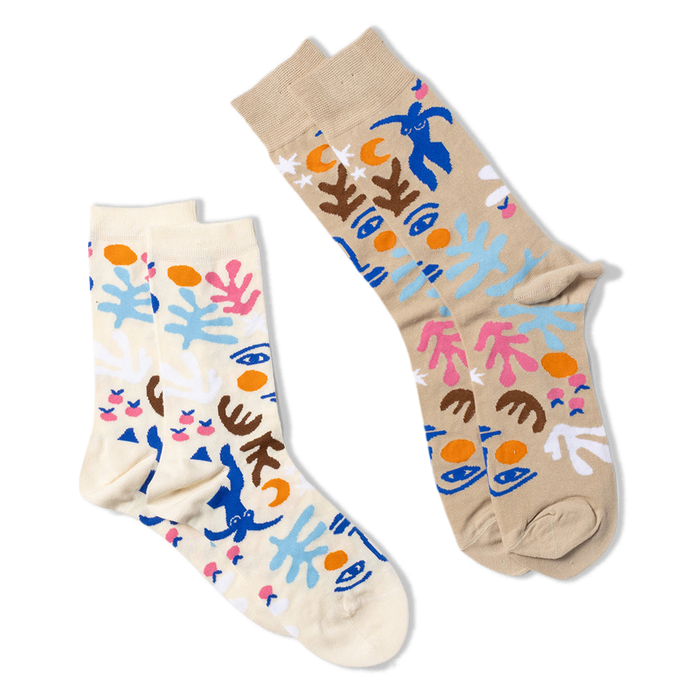 Two pairs of abstract art-patterned socks. One pair is tan, the other is cream, both with blue figures, faces, and shapes.