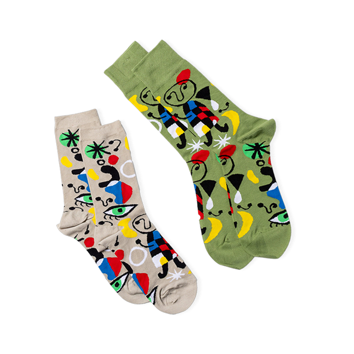 Two pairs of abstract art crew socks. One pair is olive green, the other light beige, both with colorful art patterns.