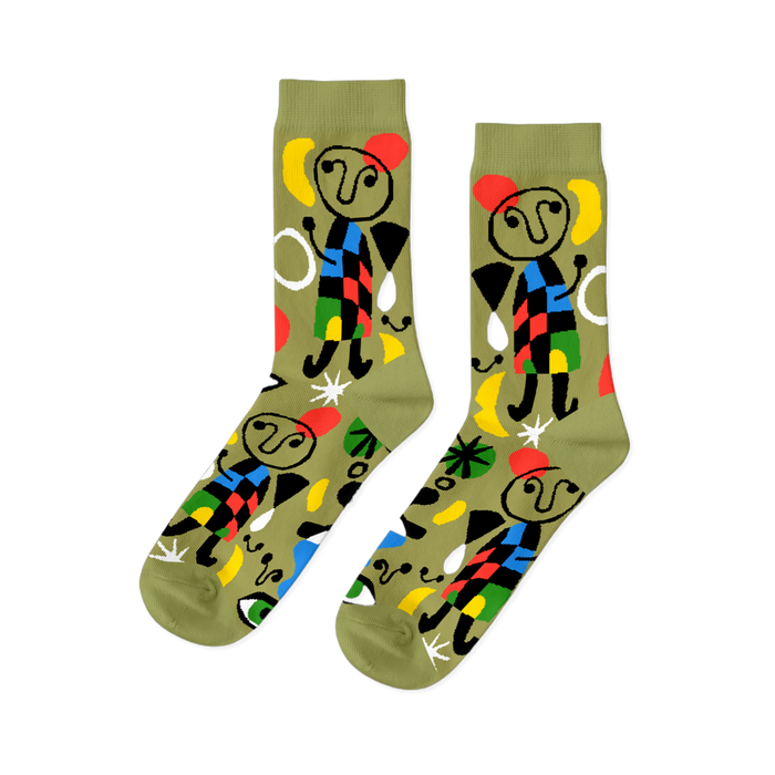 Pair of olive green crew socks with abstract art pattern, featuring stick figures, red stars, yellow moons, and colorful geometric shapes.