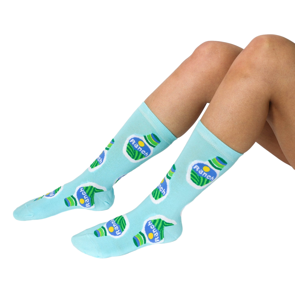 A person's legs are shown wearing light blue crew socks with a ranch dressing bottle pattern on a white background.