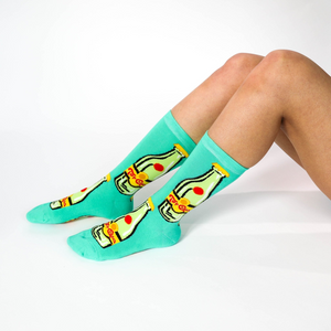 A person's lower legs and feet, wearing the aqua Top Chica bottle crew socks, sitting on a white surface.