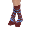 A person's bare legs wearing reddish-brown snake pattern crew socks, with ankles crossed, against a plain background.