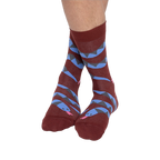A person's bare legs wearing reddish-brown snake pattern crew socks, with ankles crossed, against a plain background.