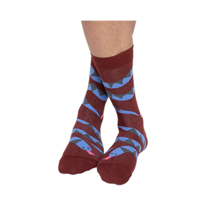 A person's bare legs wearing reddish-brown snake pattern crew socks, with ankles crossed, against a plain background.