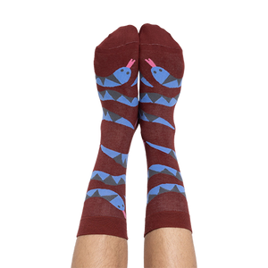 A person's bare legs wearing reddish-brown snake pattern crew socks, shown from the soles up, against a plain background.