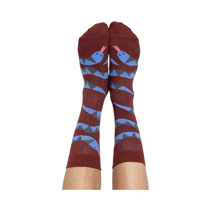 A person's bare legs wearing reddish-brown snake pattern crew socks, shown from the soles up, against a plain background.