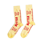 A pair of light yellow ankle socks printed with 'BUTTER' and 'NET WT. 4 OZ. (113g)' in red text, mimicking a stick of butter wrapper.