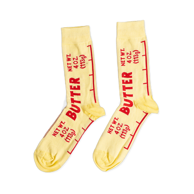 A pair of light yellow ankle socks printed with 'BUTTER' and 'NET WT. 4 OZ. (113g)' in red text, mimicking a stick of butter wrapper.
