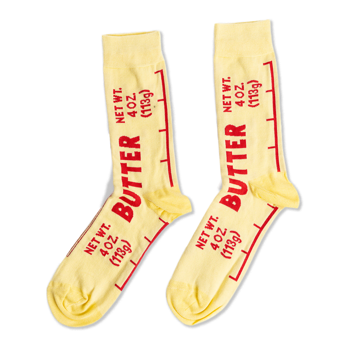 A pair of light yellow ankle socks printed with 'BUTTER' and 'NET WT. 4 OZ. (113g)' in red text, mimicking a stick of butter wrapper.