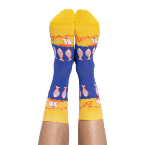 A person's feet wearing the blue and yellow anchovy crew socks, with the pattern of fish and text clearly visible.