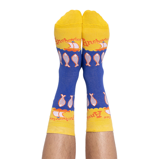 A person's feet wearing the blue and yellow anchovy crew socks, with the pattern of fish and text clearly visible.
