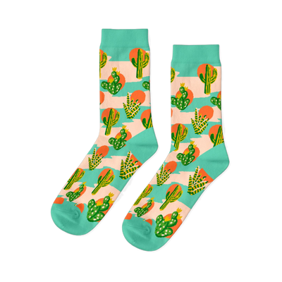 Pair of crew socks with a desert theme. Features green saguaro and prickly pear cacti, orange suns, on a peach-pink and mint green striped background.